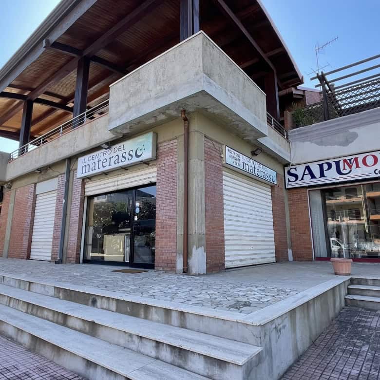 Pannello frontale di un edificio commerciale con negozi in vendita o affitto, con ampie vetrine e accesso tramite scalinate, situato in un'area urbana moderna e ben sviluppata.