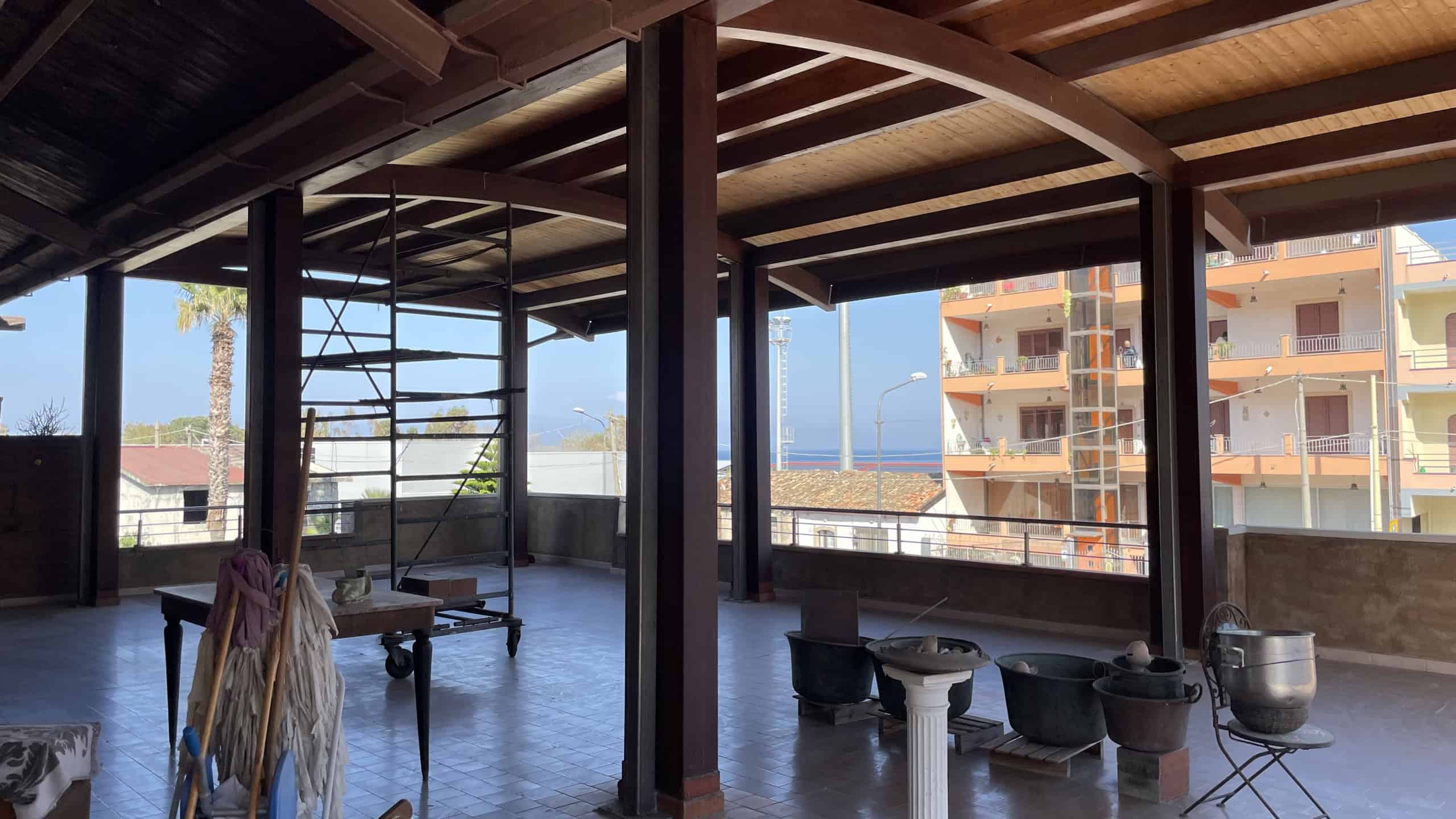 Ampio terrazzo coperto con vista sul mare e sulle palazzine circostanti, struttura in legno e metallo, ideale per relax e socializzazione all'aperto.