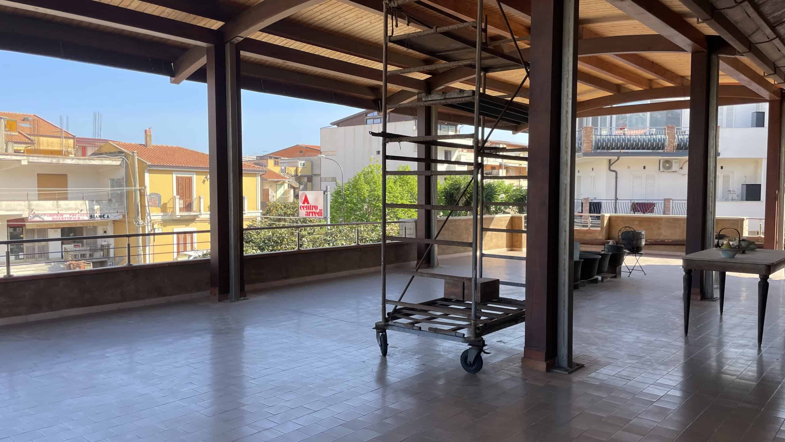 Ampio spazio interno di un appartamento in fase di ristrutturazione con scaffalature mobili e grandi finestre che offrono luce naturale e vista sulla città.