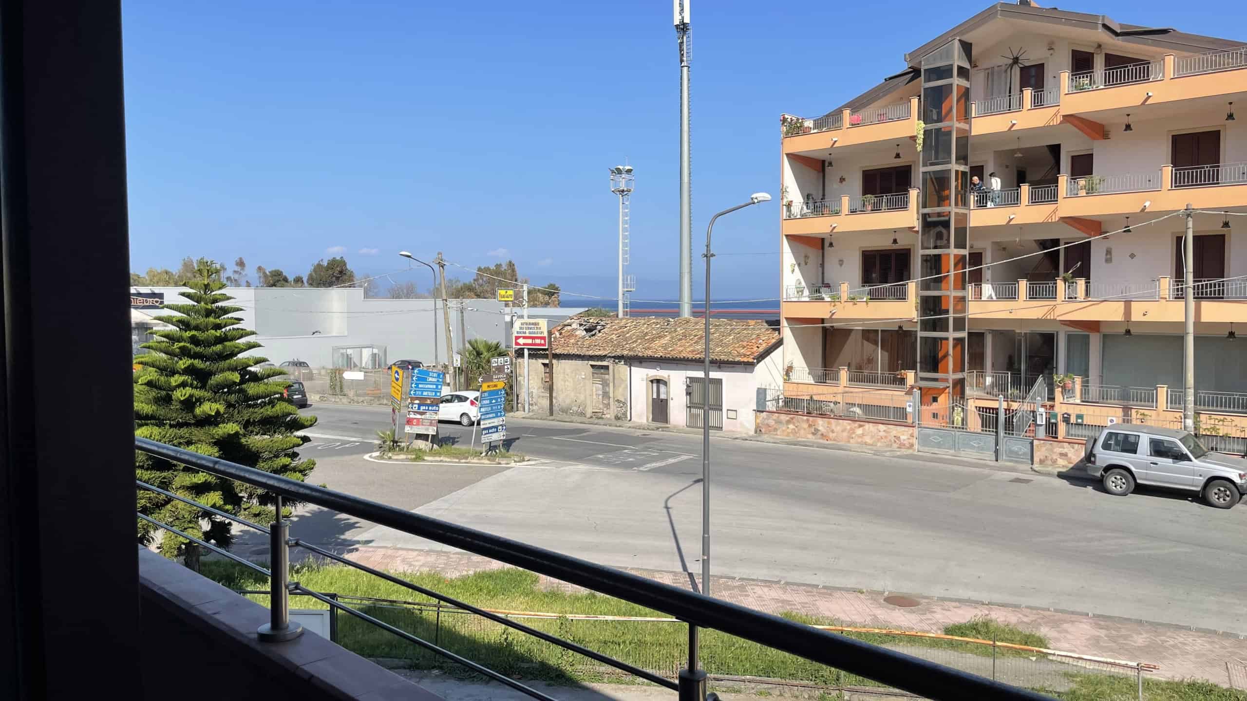 Vista panoramica di un quartiere residenziale con edifici moderni e strada trafficata, vista mare sullo sfondo, in una giornata soleggiata.