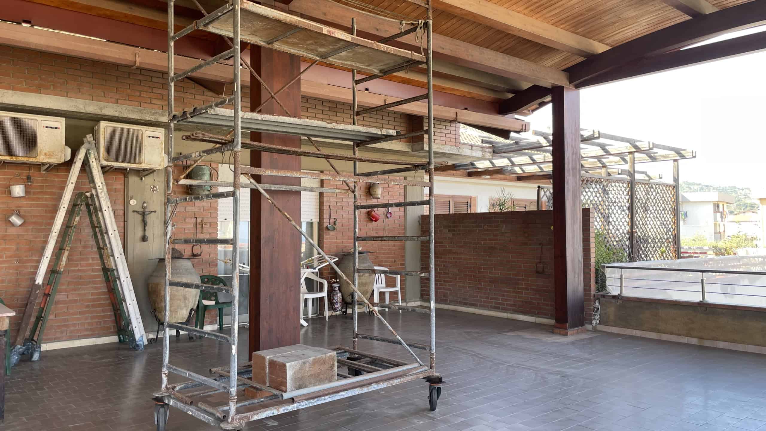 Lavori di costruzione su un balcone o terrazza con struttura in acciaio e legno, scaffalature e attrezzi da lavoro.