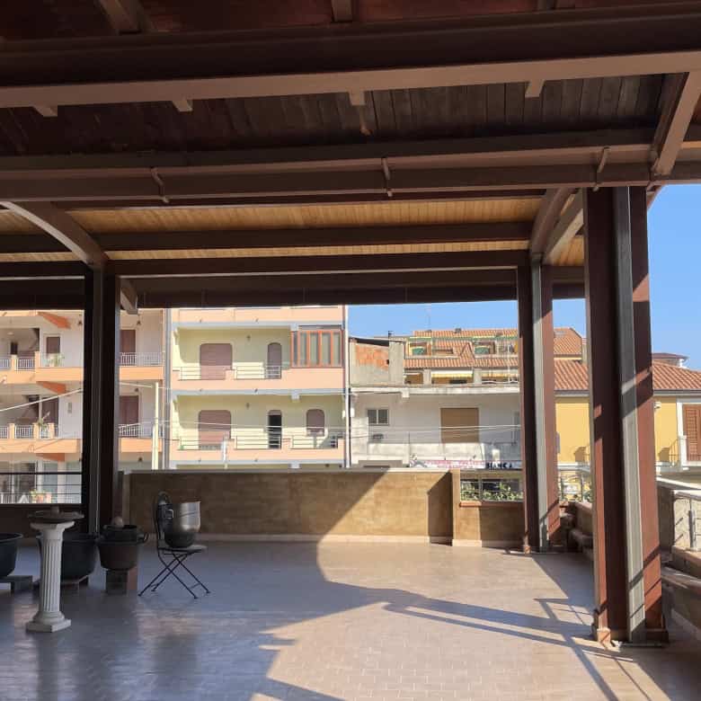 Ampia terrazza coperta con vista su edifici residenziali, ideale per relax e socializzazione all'aperto, con spazio per mobili da esterno e piante ornamentali.