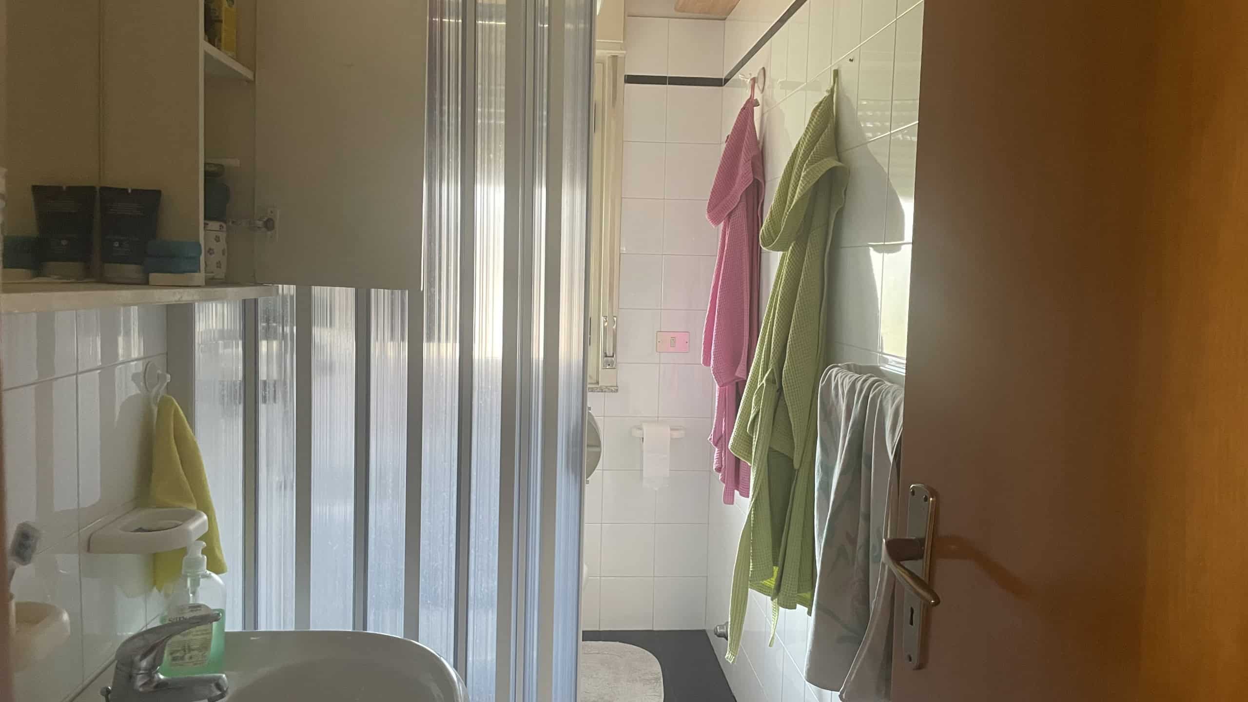 Lavatrice e asciugamani colorati appesi in bagno, ambiente luminoso e pulito, ideale per servizi di lavanderia e cura della casa.