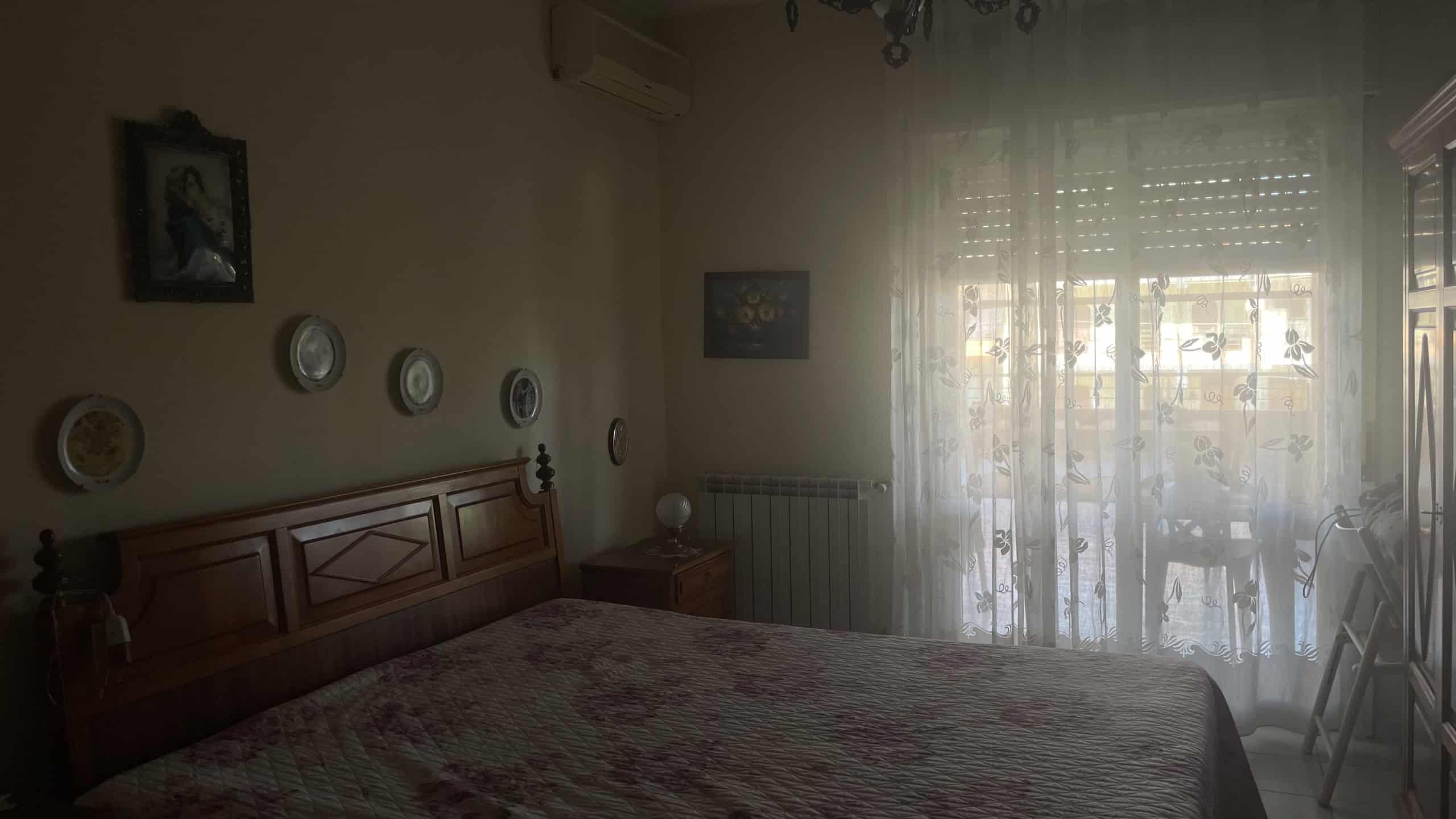 Letto matrimoniale in camera da letto con pareti decorate, tende trasparenti e luce naturale, ambiente accogliente e tranquillo.