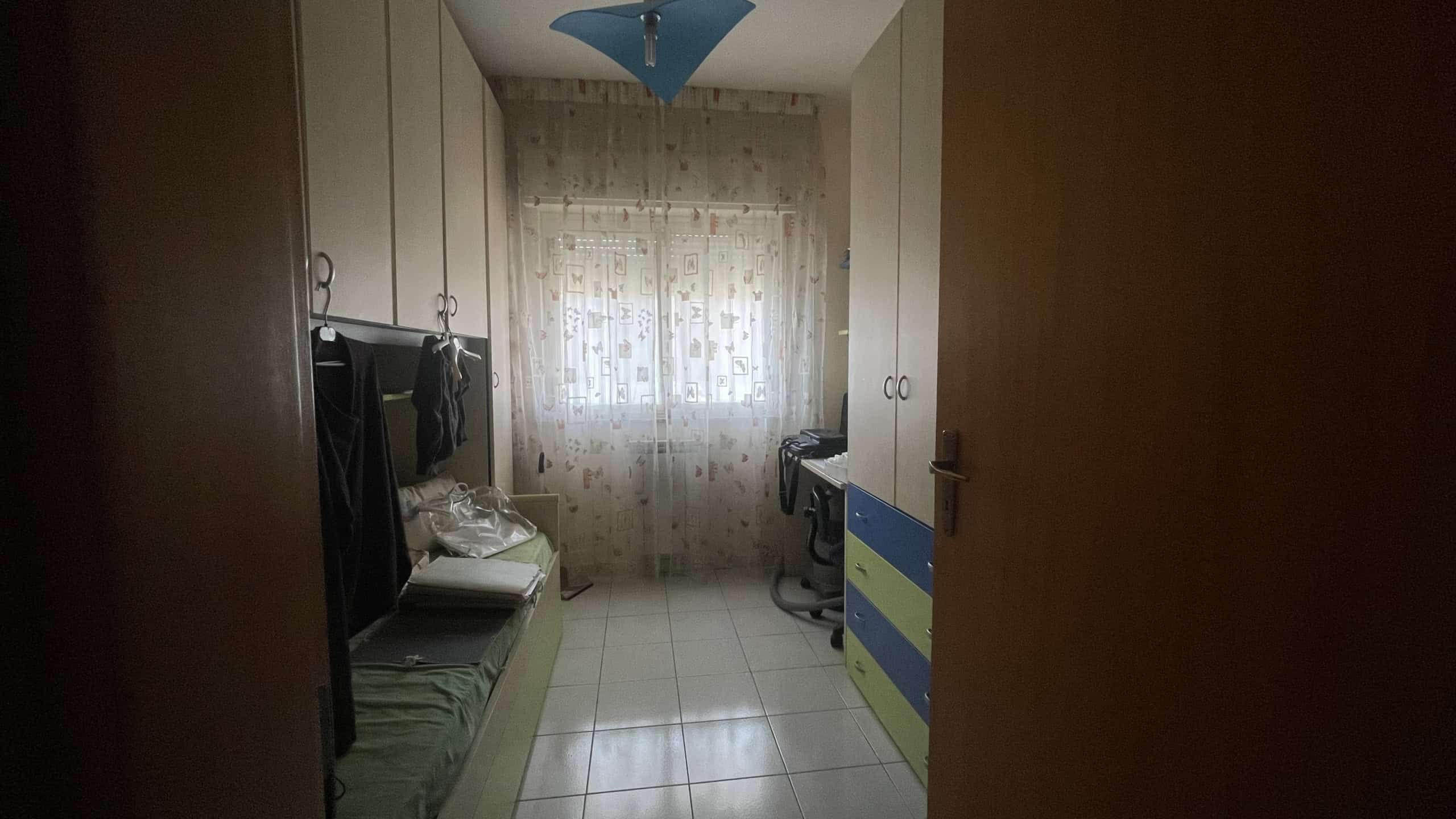 Armadio e mobili in una stanza luminosa con finestra, arredamento funzionale e spazio ordinato, ideale per uso domestico o ufficio.