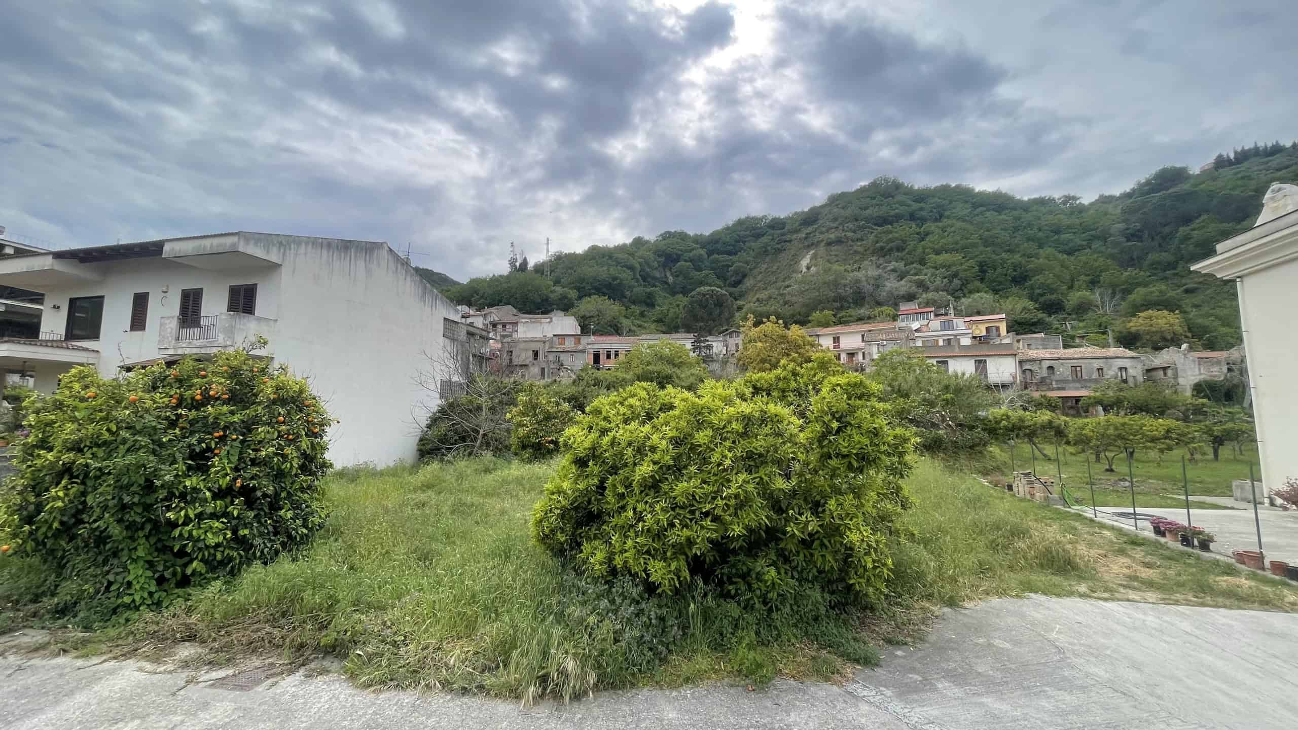 Ampia area verde con arbusti e case residenziali in collina, vista panoramica su un paesaggio naturale e urbano, ideale per investimenti immobiliari e sviluppo di progetti residenziali in zona tranqui.