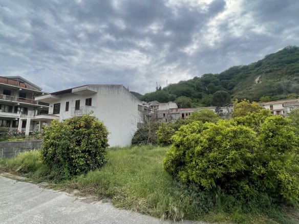 Terreno edificabile in zona residenziale con case moderne e natura circostante, situato ai piedi di una collina verdeggiante, ideale per costruzioni e investimenti immobiliari in Italia.