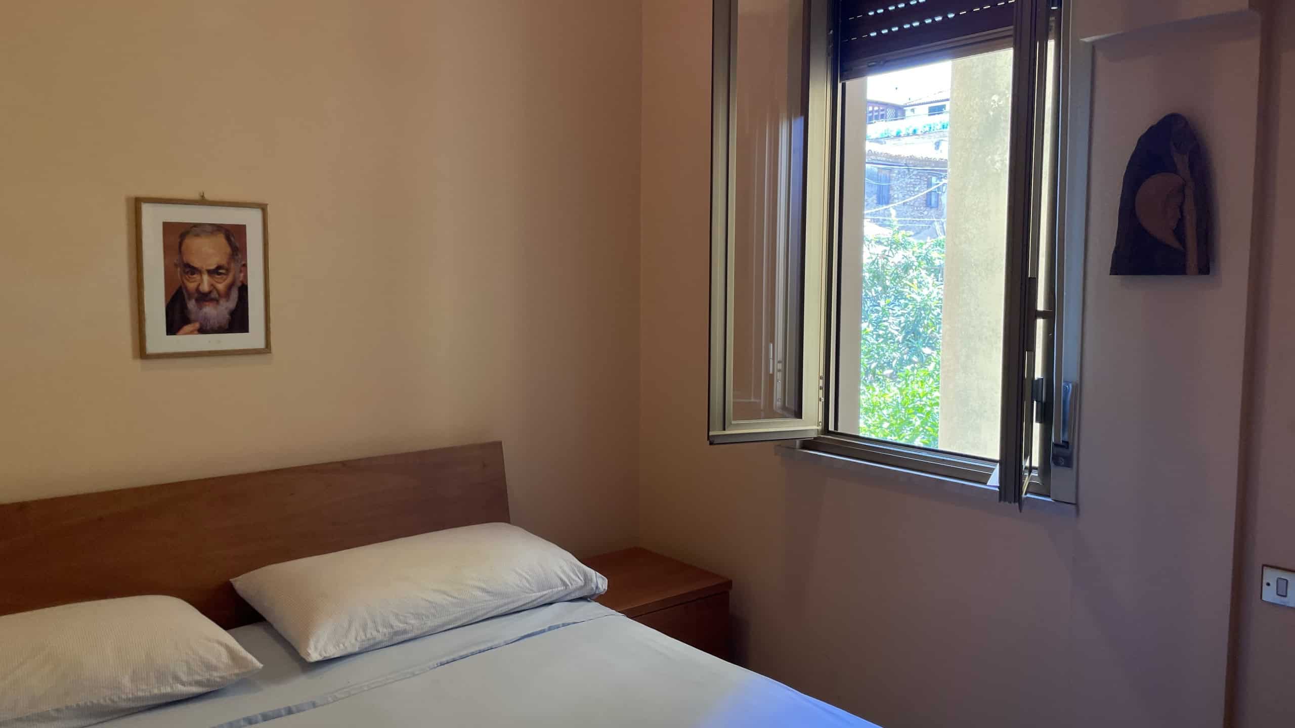 Ampia camera da letto con finestra aperta, vista su giardino e natura, arredi moderni e atmosfera luminosa, ideale per case in vendita o affitto a NextCasa.