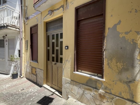 Ampia immagine di una facciata di edificio residenziale in stile italiano con pareti gialle e dettagli in pietra, portone d'ingresso e finestre con tapparelle in posizione abbassata.