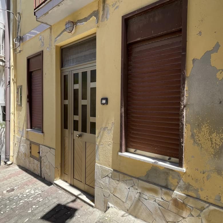 Ampia immagine di una facciata di edificio residenziale in stile italiano con pareti gialle e dettagli in pietra, portone d'ingresso e finestre con tapparelle in posizione abbassata.