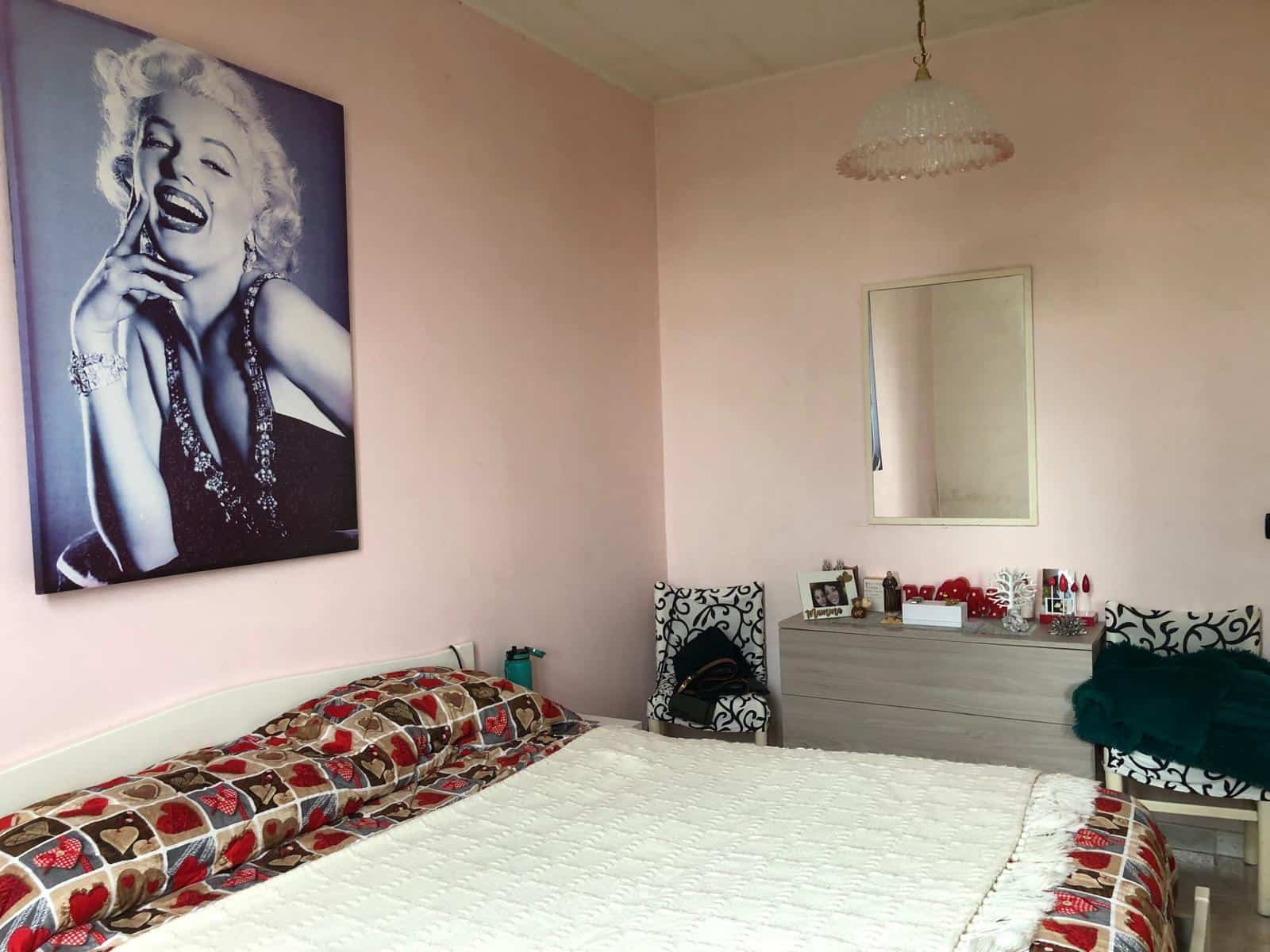 Letto matrimoniale con copriletto decorativo in una camera da letto moderna, decorata con un quadro iconico di Marilyn Monroe e mobili eleganti. Ambiente luminoso e accogliente, ideale per soggiorni c.