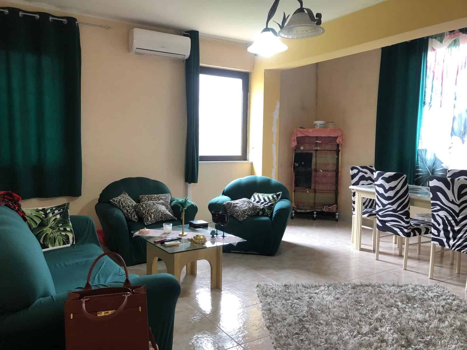 Interno soggiorno con divani verdi, tavolino e zona pranzo con sedie zebra, luce naturale e aria condizionata, ambiente accogliente e luminoso.