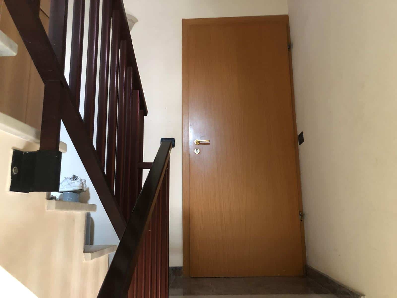 Pulsante di uscita di emergenza vicino a una porta in un ambiente interno, con ringhiera in legno e pareti bianche, in un'area di passaggio di una casa o appartamento.