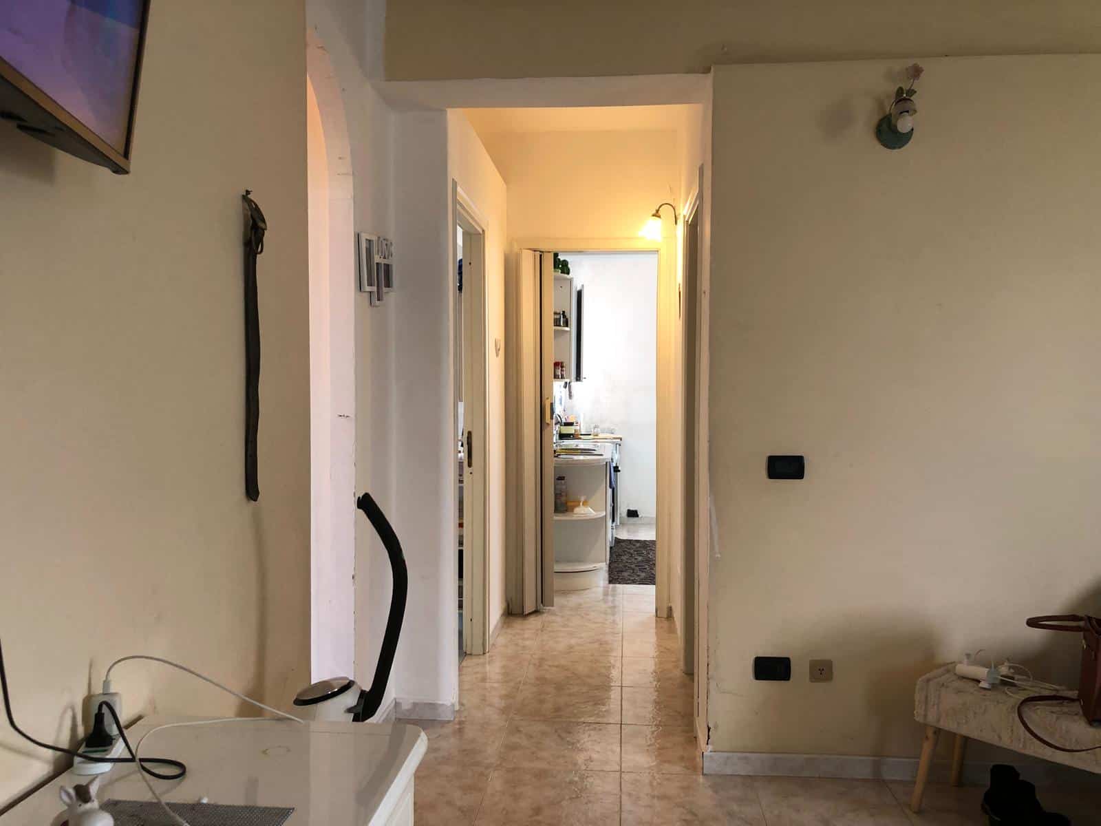 Interno di un appartamento con corridoio e ingresso alla cucina, arredato in stile moderno, con pareti chiare e pavimento in marmo.