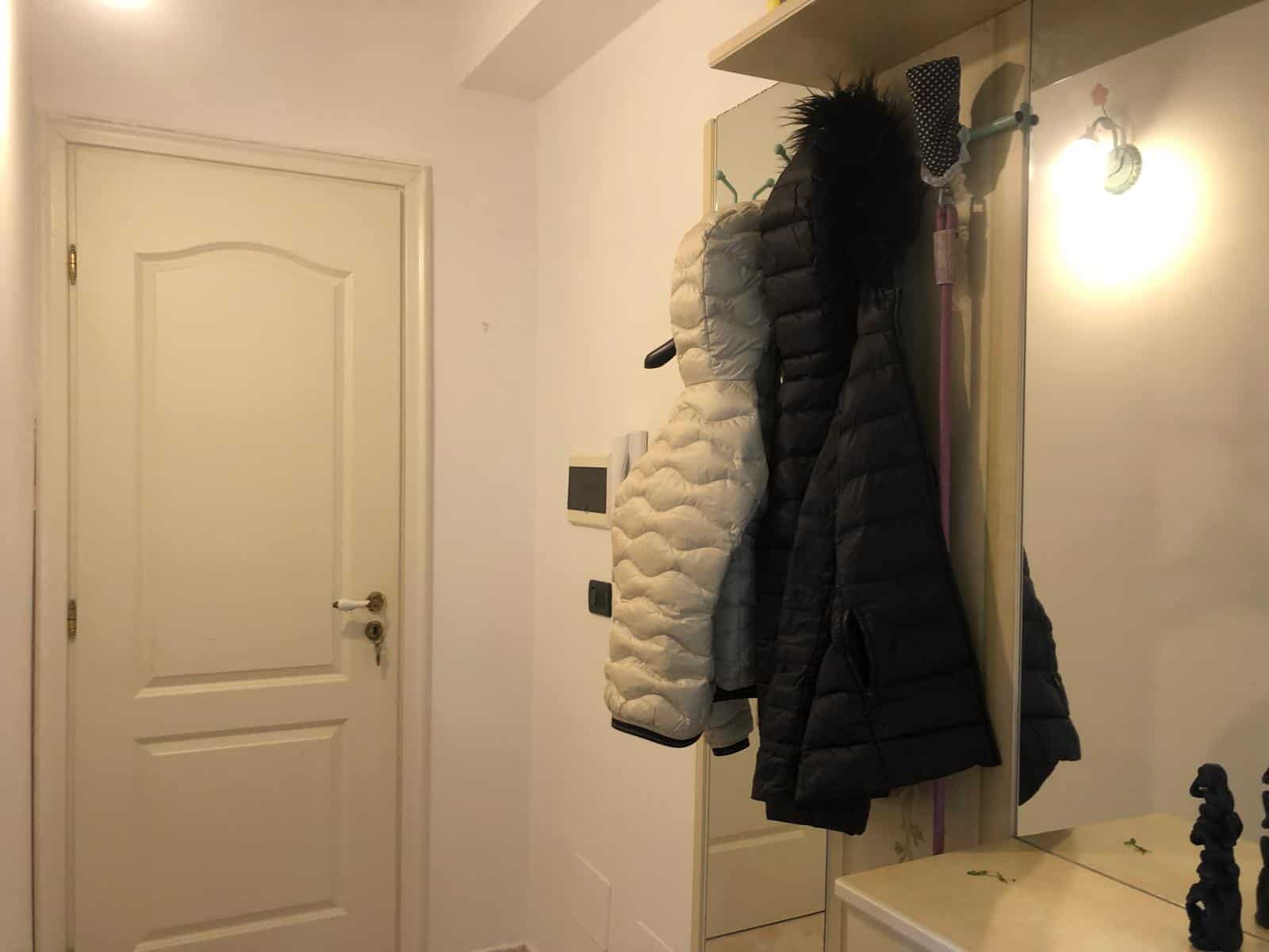 Panchetto porta cappotti con ganci e cappotti invernali appesi, ingresso di casa elegante e funzionale.