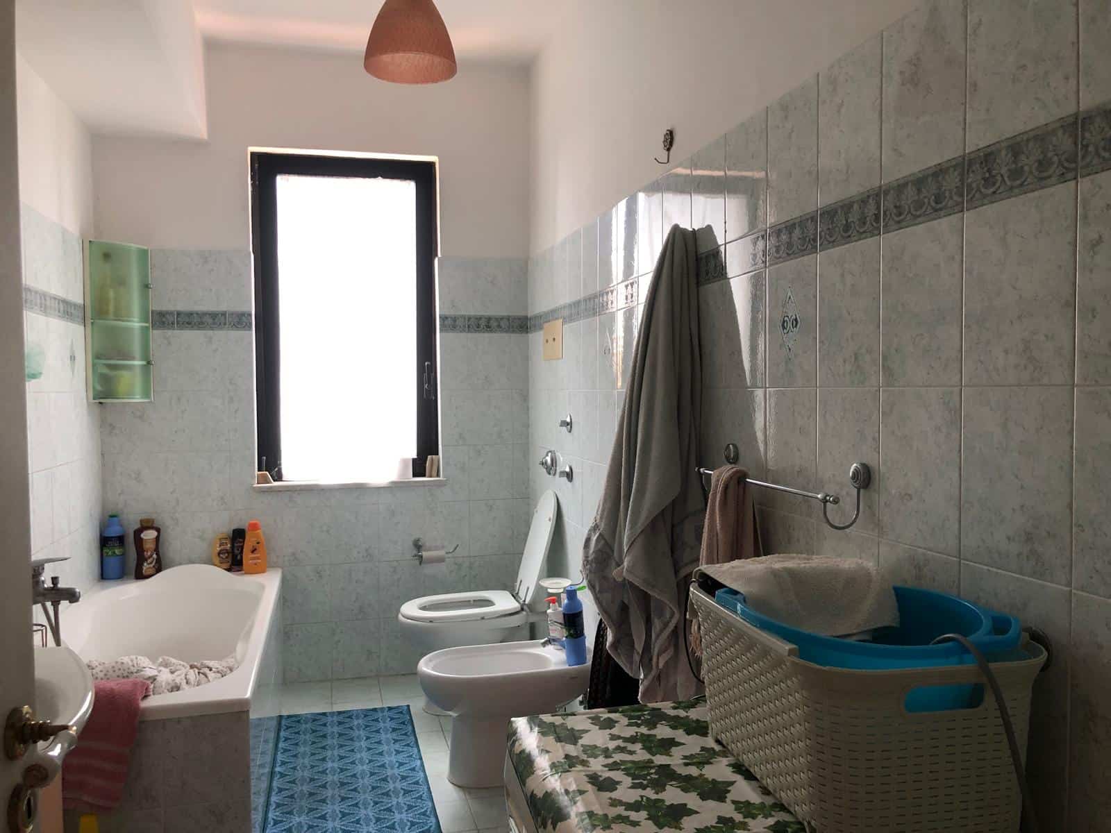 Lavabo e bidet in un bagno con pareti rivestite di piastrelle azzurre e finestra con luce naturale.