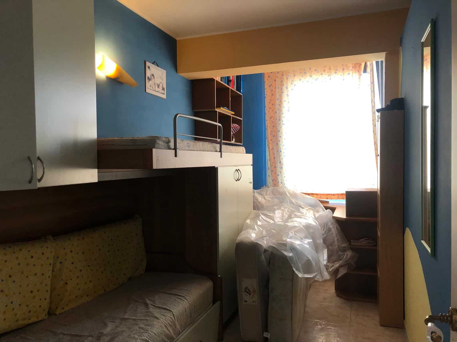 Camera da letto in appartamento con letto a soppalco, pareti blu e arredi moderni, luce naturale dalla finestra, ideale per affitti turistici o residenziali a NextCasa.