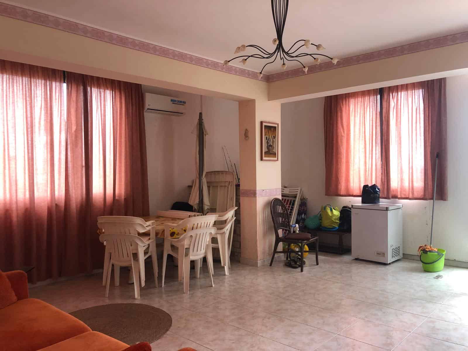 Ampia sala soggiorno con tende rosa, area pranzo con tavolo e sedie, spazio relax con poltrona e frigorifero, ambiente luminoso e accogliente.