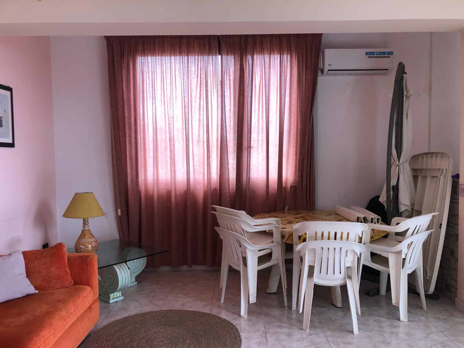Interno soggiorno con tavolo da pranzo, sedie bianche, divano arancione, lampada da tavolo e aria condizionata, ambiente luminoso e accogliente.
