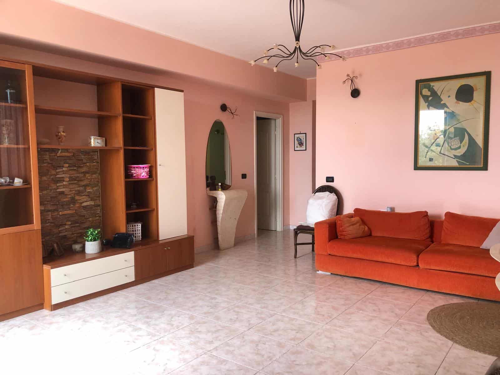 Appartamento spazioso con soggiorno arredato con divano rosso e parete decorativa in stile moderno, illuminato da lampadario centrale e luce naturale dalla finestra.