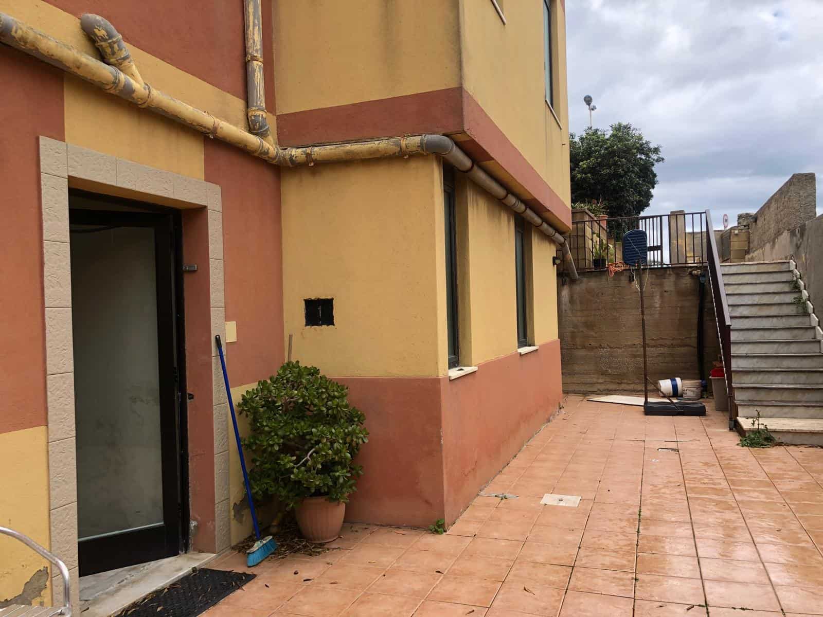 Spazio esterno di un appartamento con terrazza pavimentata, piante e scale in pietra, vista su un cielo nuvoloso, ideale per relax e socializzazione.