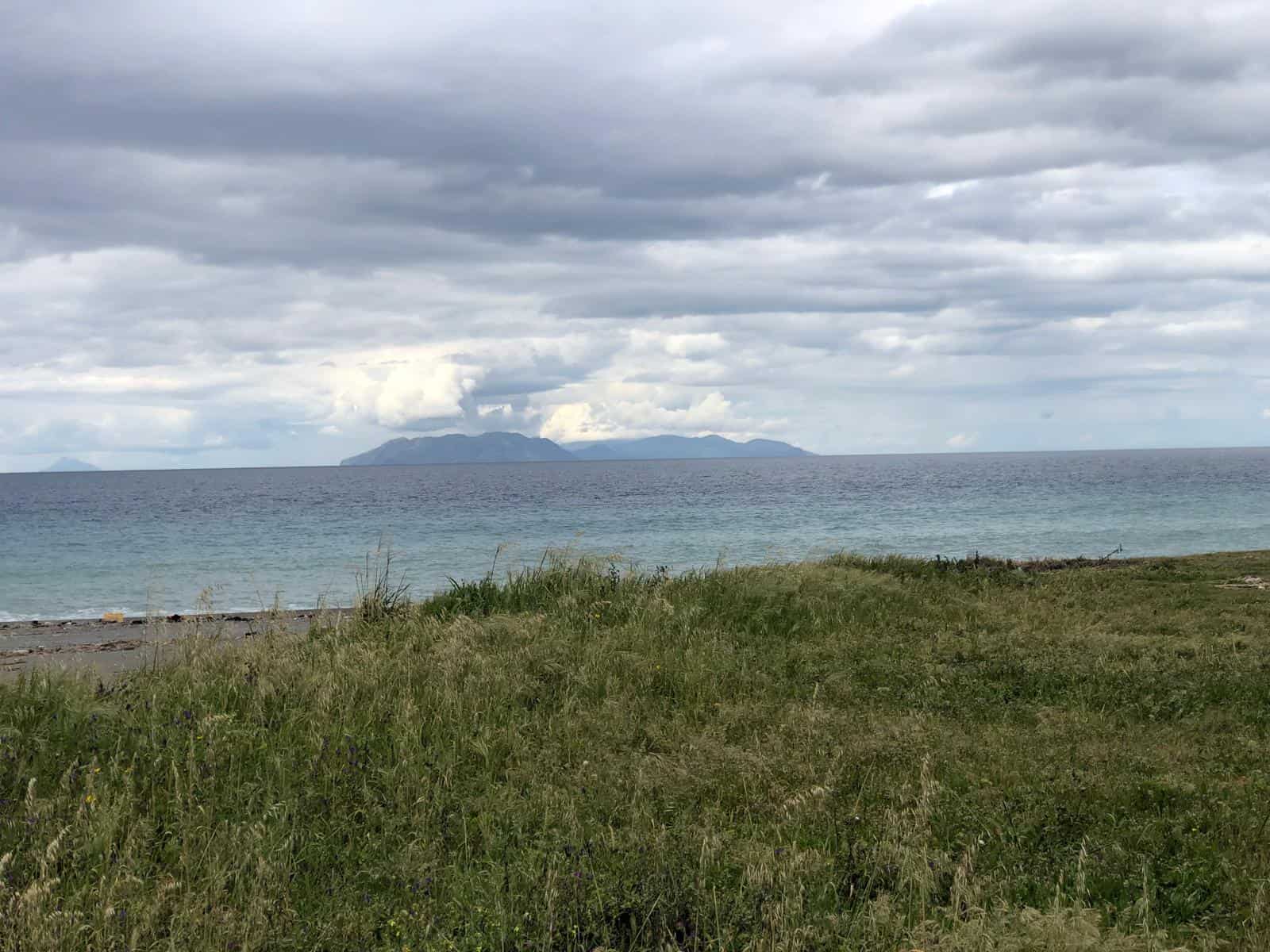 Verde prato vicino alla spiaggia con vista sull'oceano e isole lontane sotto un cielo nuvoloso, ideale per case al mare e proprietà fronte mare in Italia.