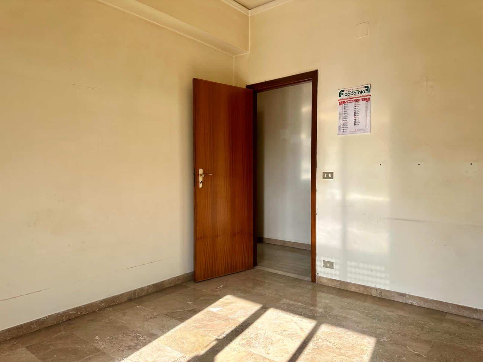 Stanza vuota con porta in legno e pareti beige, illuminata dalla luce naturale, ideale per affitto o vendita immobiliare.