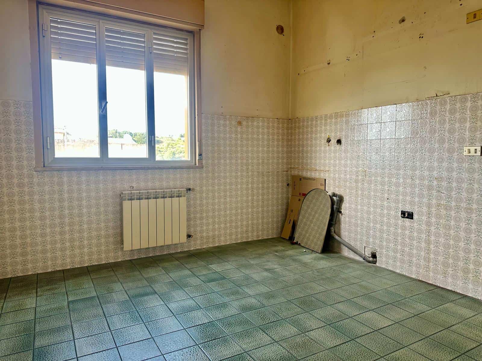 Lavagna di cucina vuota con pareti rivestite in piastrelle e finestra che lascia entrare luce naturale, pronta per essere ristrutturata o personalizzata. Ideale per progetti di ristrutturazione abitat.