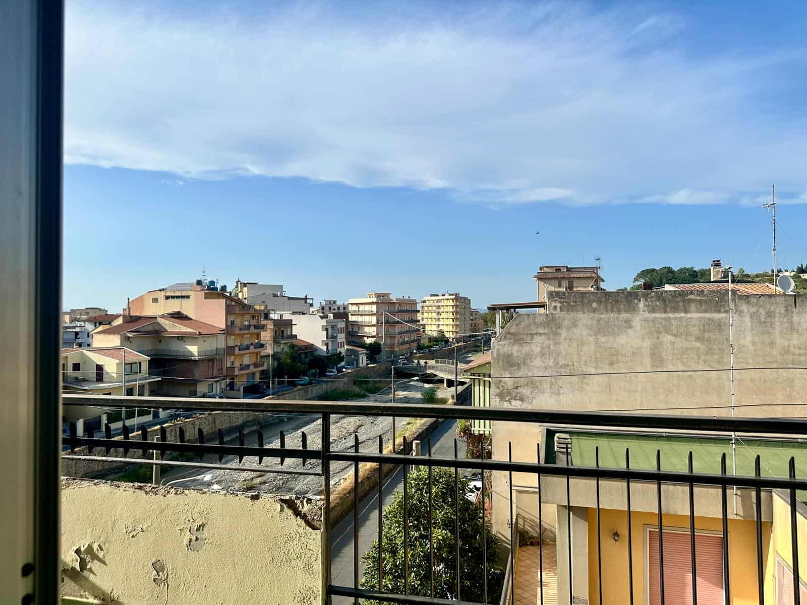 Balcone con vista su quartiere urbano, edifici residenziali e cielo sereno, in un'immagine di NextCasa che evidenzia l'ambiente cittadino e l'architettura moderna.