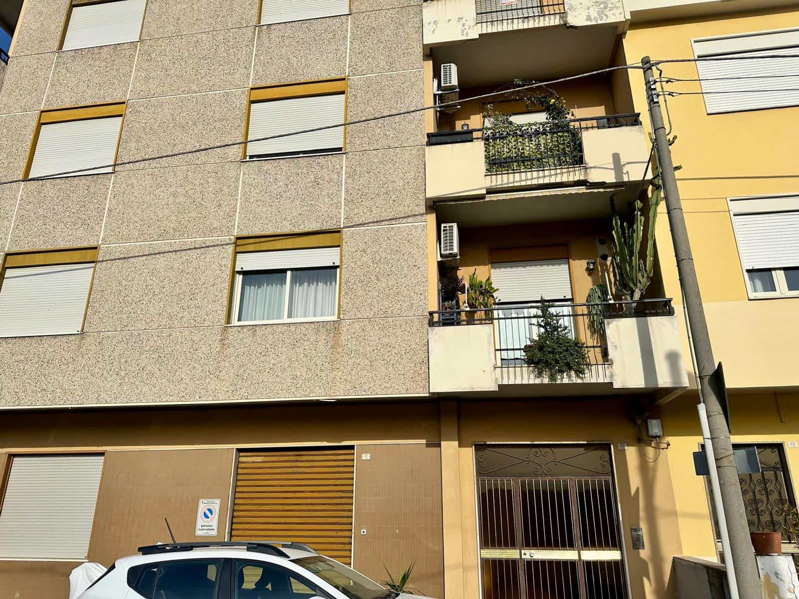 Facciata di un edificio residenziale con balconi e piante, vista dall'esterno, in un quartiere urbano.