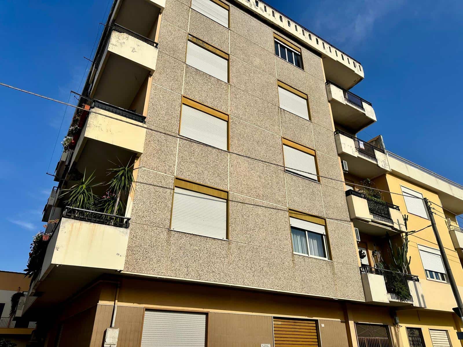 Edificio residenziale moderno con balconi e finestre, facciata in cemento e dettagli in legno, situato in zona urbana soleggiata.