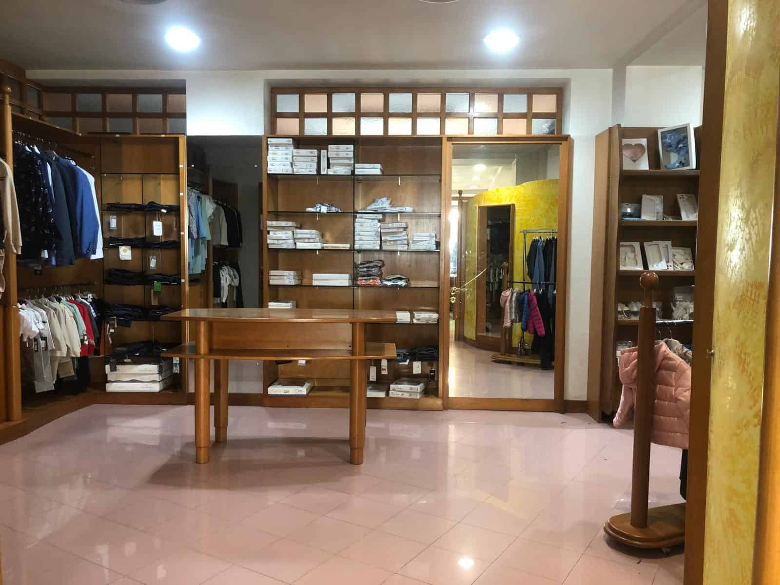 Vetrina di negozio di abbigliamento con scaffali e armadi pieni di vestiti e accessori, ambiente ben illuminato e accogliente.