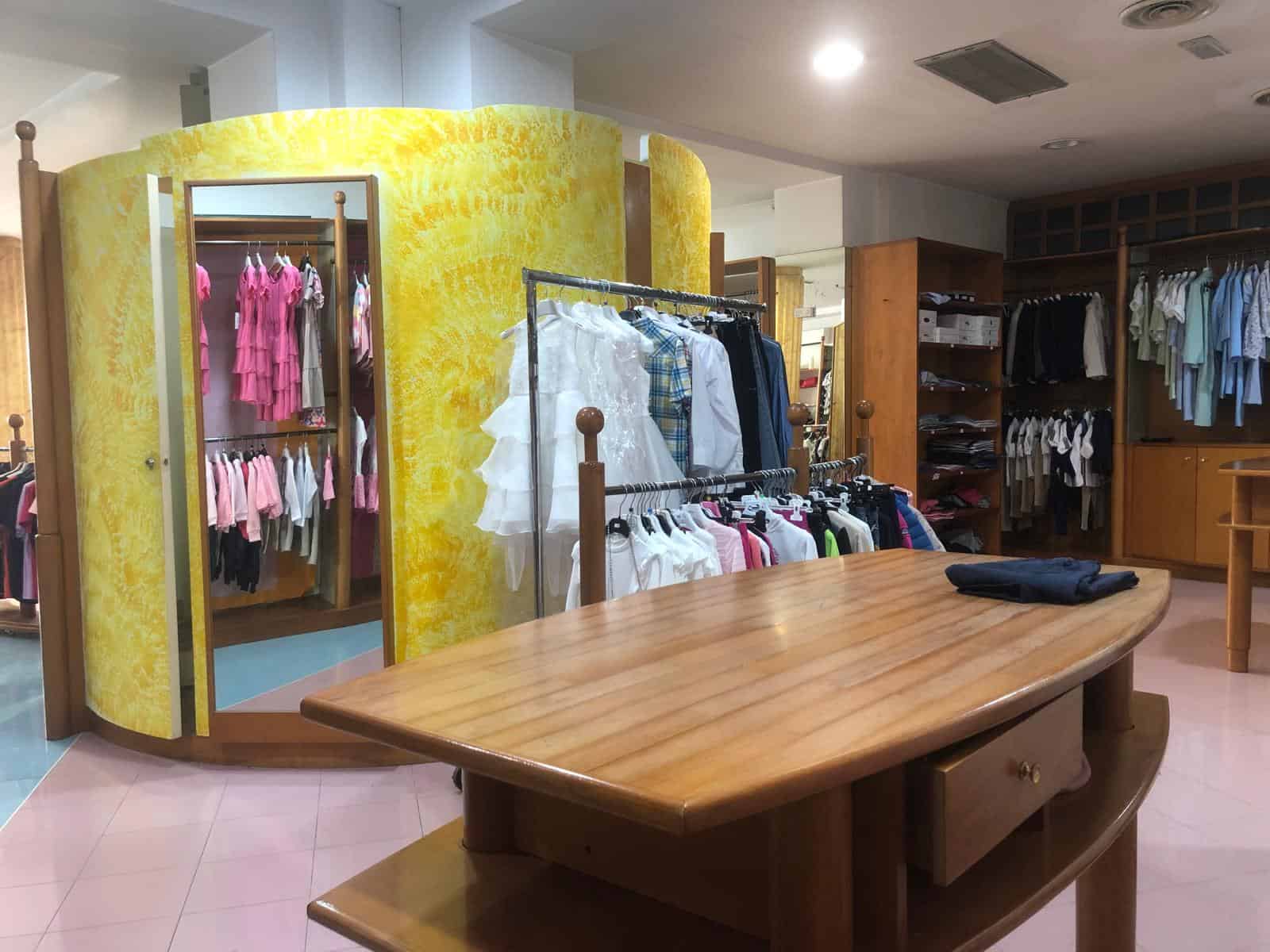 Vestiti donna in negozio di abbigliamento, esposizione di abbigliamento femminile in un negozio di moda NextCasa, con pareti gialle e scaffali di legno.