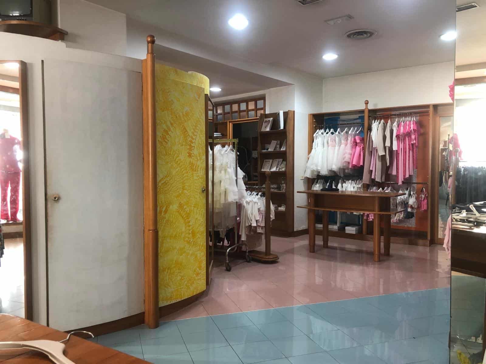 Vestito da bambino in negozio di abbigliamento per neonati, esposizione di vestiti rosa e bianchi, scaffali con abbigliamento e accessori per neonati, ambiente accogliente e ben illuminato.
