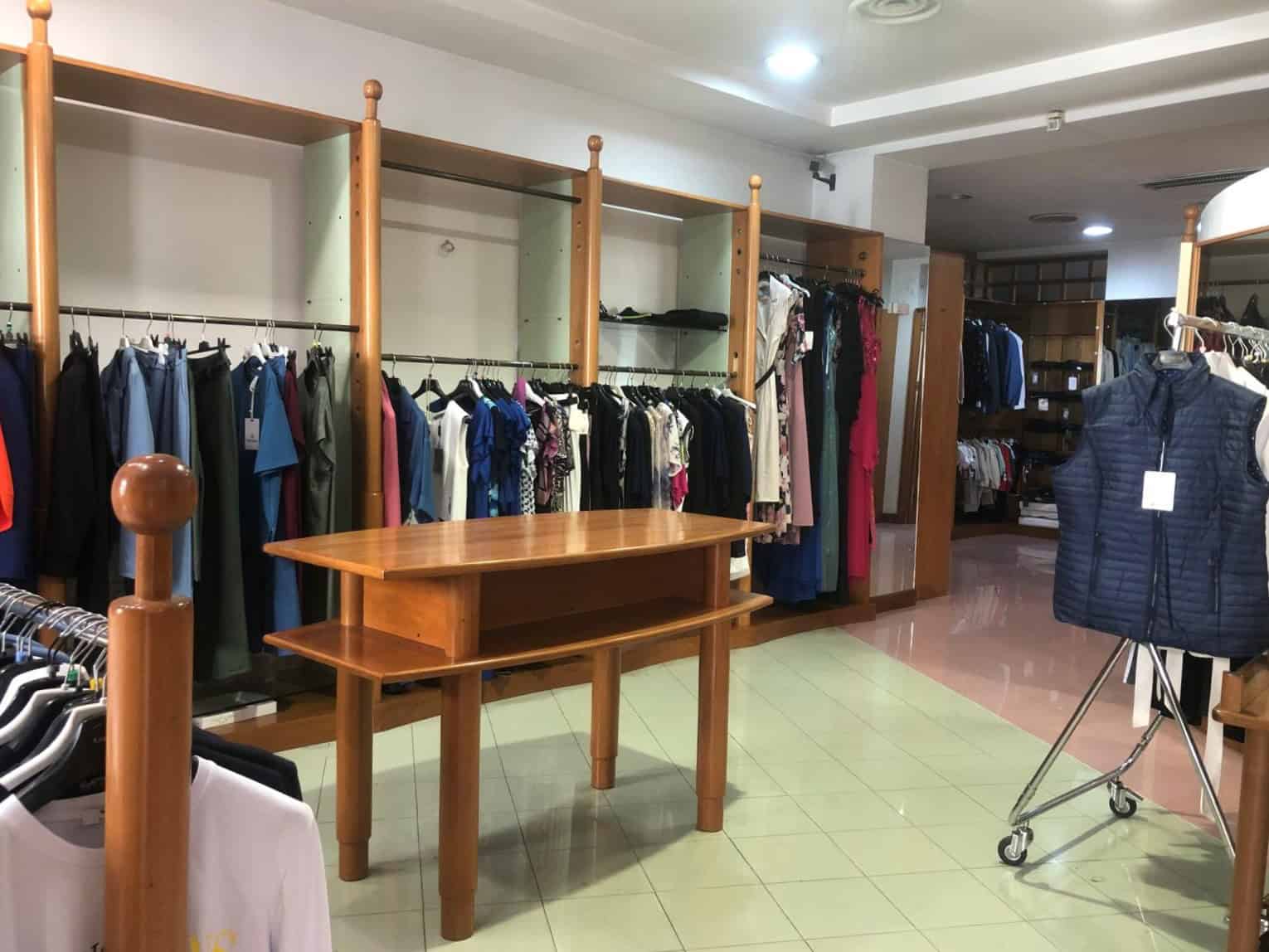 Vestiti e capi di abbigliamento in vendita in un negozio di moda con scaffali e appendiabiti in legno, ambiente ben illuminato e organizzato per lo shopping.