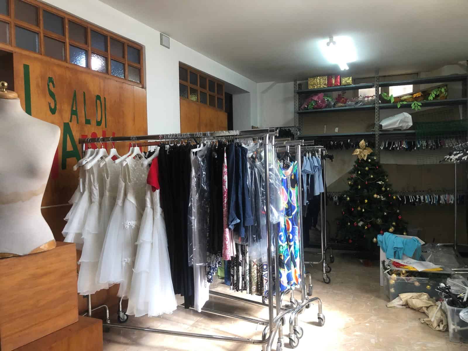 Abilmente esposta in negozio di abbigliamento con vestiti eleganti e da cerimonia, tra cui abiti da sposa e abiti da sera, con decorazioni natalizie sullo sfondo.