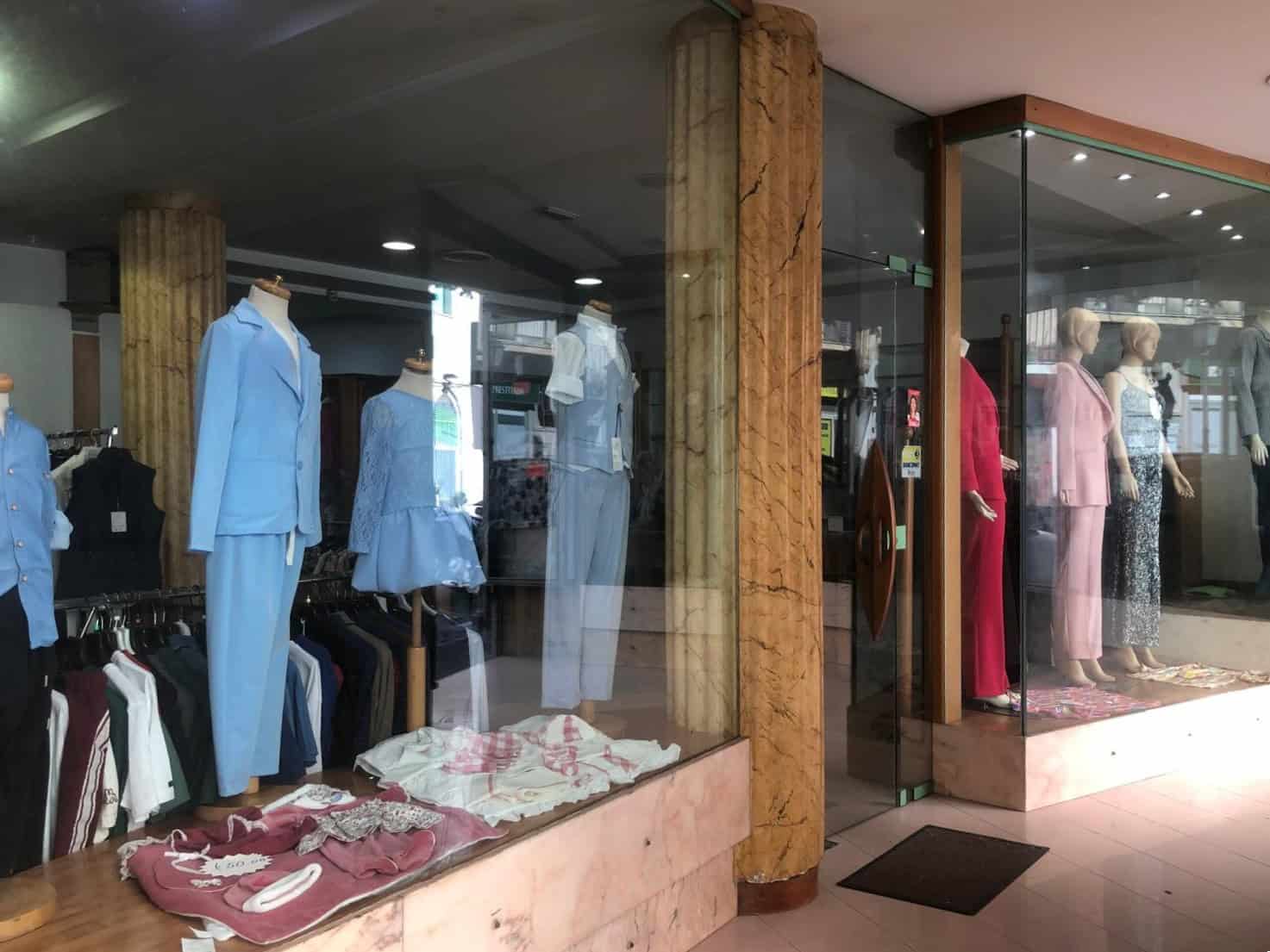 Vestiti eleganti e casual esposti in vetrina di un negozio di abbigliamento, con manichini che indossano abiti color pastello e accessori coordinati, all’interno di un ambiente moderno e ben illuminat.