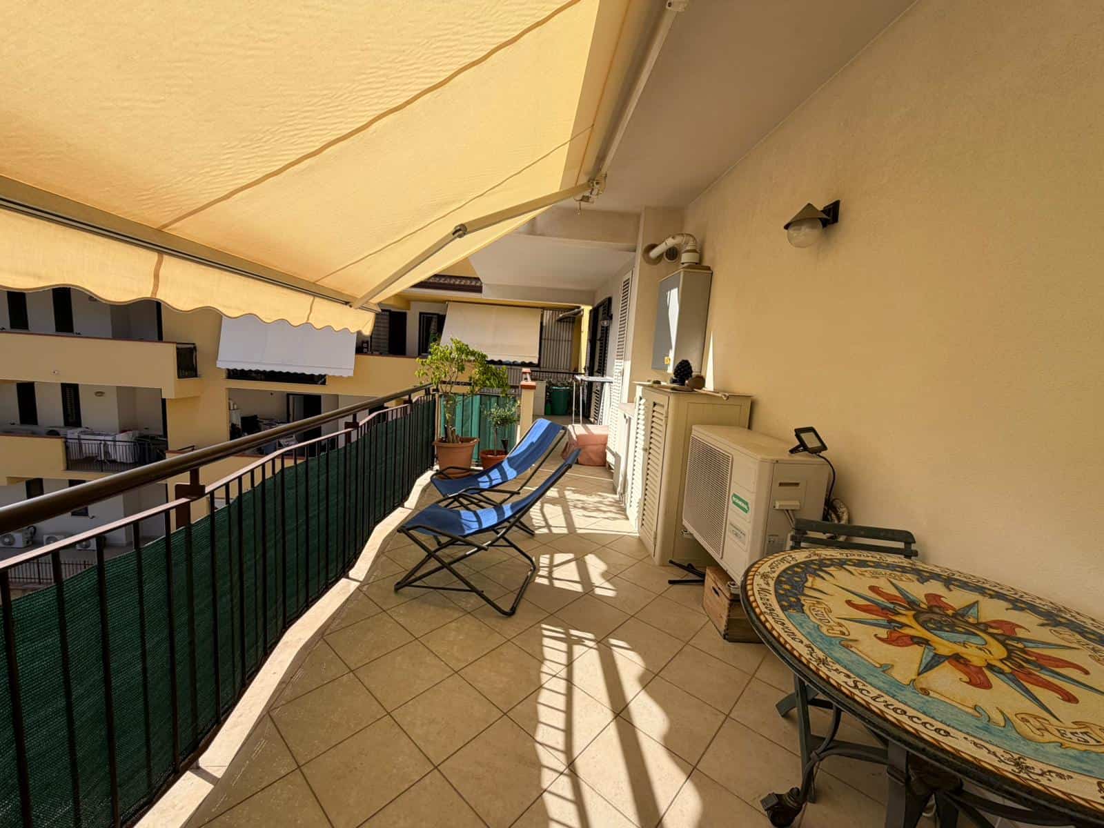 Balcone di un appartamento con tende parasole, sedie e vista sulle case vicine, ideale per relax e svago all'aperto.