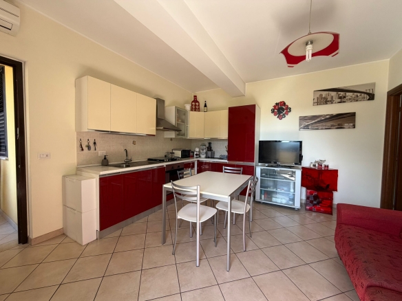 Una cucina moderna e accogliente con mobili bianchi e rossi, area pranzo con tavolo e sedie, soggiorno con TV e divano rosso, decorazioni eleganti e illuminazione luminosa in un appartamento luminoso.