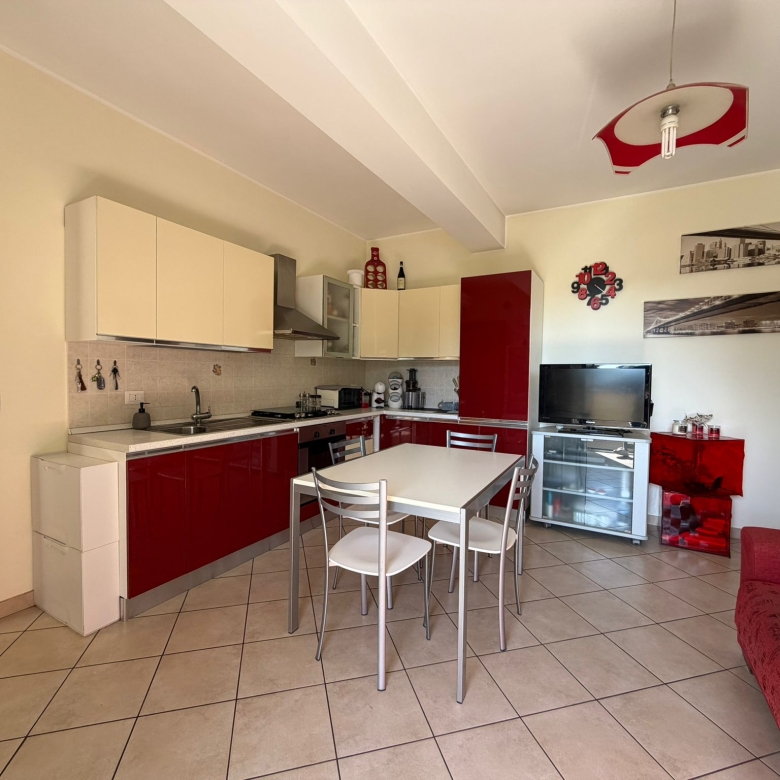 Una cucina moderna e accogliente con mobili bianchi e rossi, area pranzo con tavolo e sedie, soggiorno con TV e divano rosso, decorazioni eleganti e illuminazione luminosa in un appartamento luminoso.