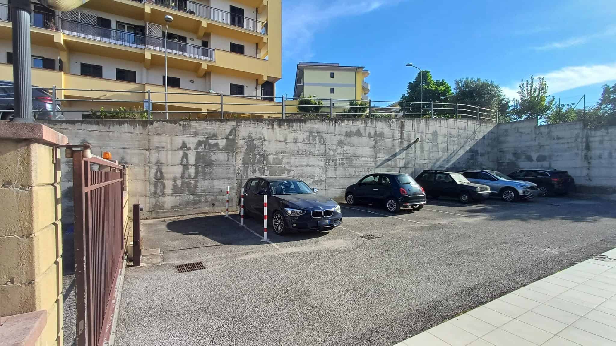 Auto parcheggio all'aperto con quattro veicoli, situato vicino a edifici residenziali in un'area urbana, sotto un cielo sereno. Ideale per residenti e visitatori che cercano un parcheggio sicuro e com.