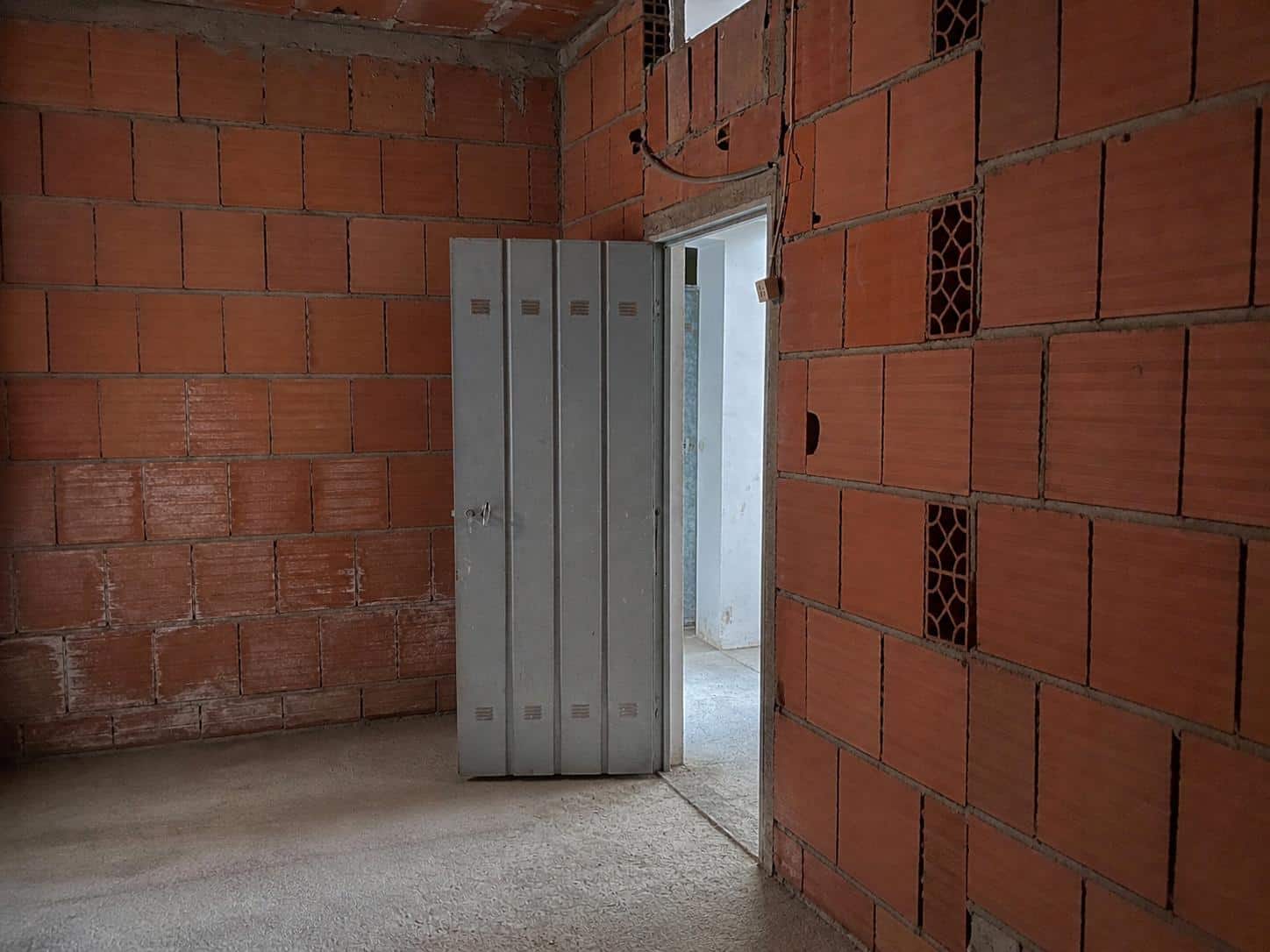 Interno di un edificio in costruzione con pareti in mattoni rossi e porta in metallo, pronto per finiture future.