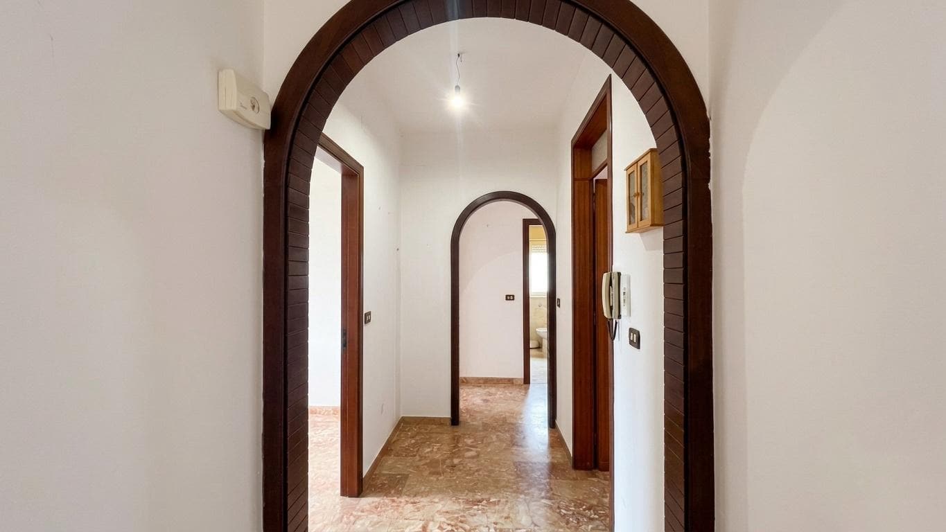 Ampia entrata con arco in legno, corridoio luminoso e porte in legno, in un appartamento elegante e ben rifinito.