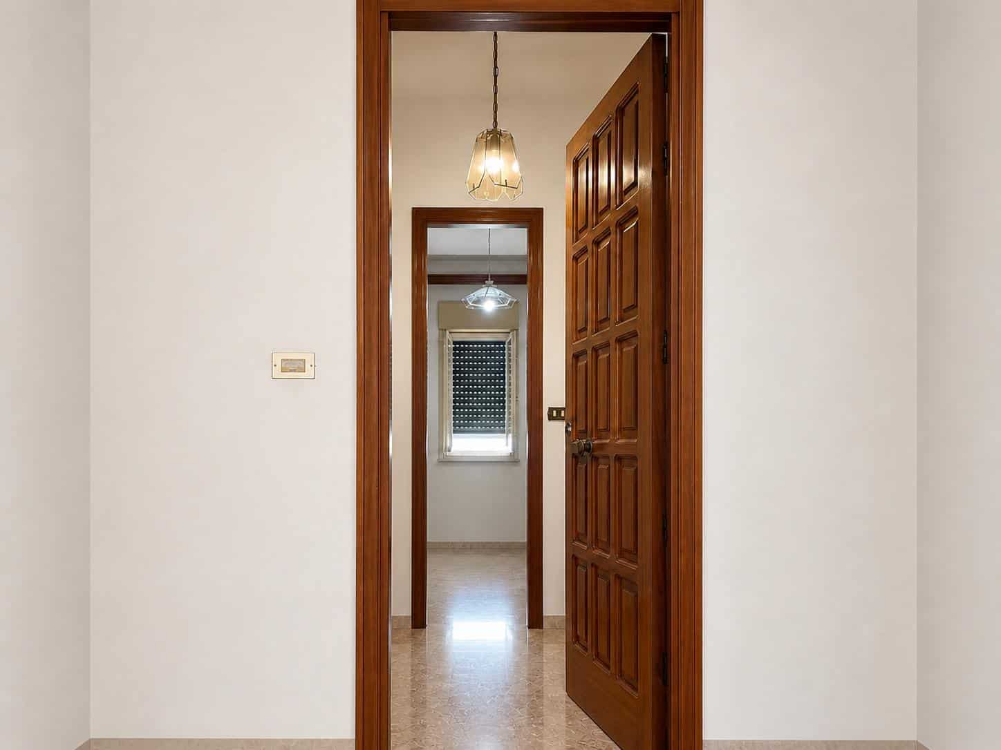 Porta in legno massiccio con dettagli eleganti, all’interno di un appartamento moderno, illuminata da una lampada a sospensione.
