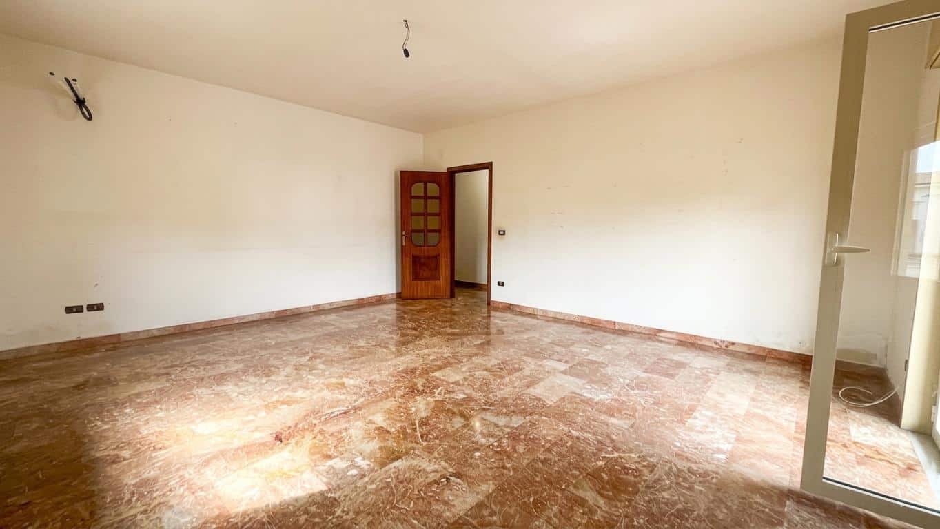 Ampia stanza vuota con pareti bianche e pavimento in marmo, pronta per essere arredata, ideale per la vendita o l'affitto di immobili residenziali.