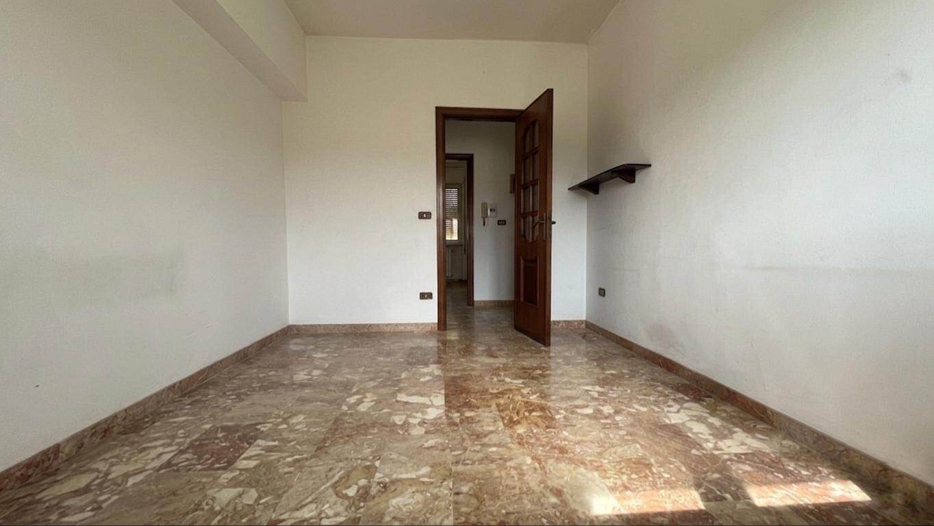 Ampia stanza vuota con pareti bianche e pavimento in marmo, pronta per essere arredata o ristrutturata, ideale per la vendita o l'affitto di immobili residenziali.