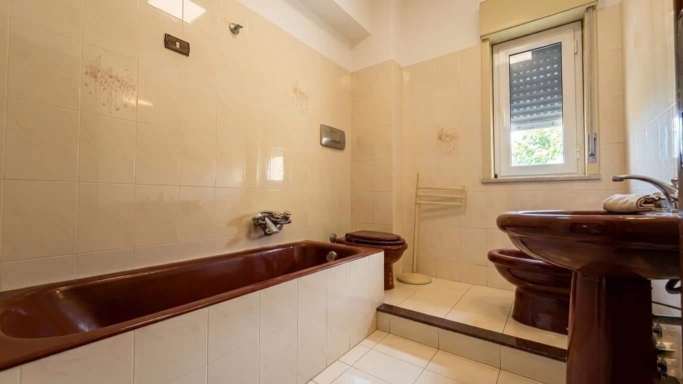 Lavabo e vasca da bagno in bagno con piastrelle beige, finestra e accessori bagno in stile classico.