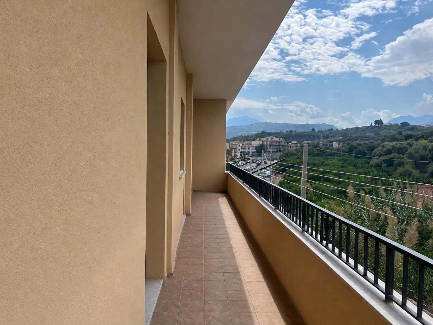 Balcone di un appartamento con vista panoramica su colline e cielo nuvoloso, in un edificio residenziale moderno, ideale per relax e godersi il paesaggio naturale.
