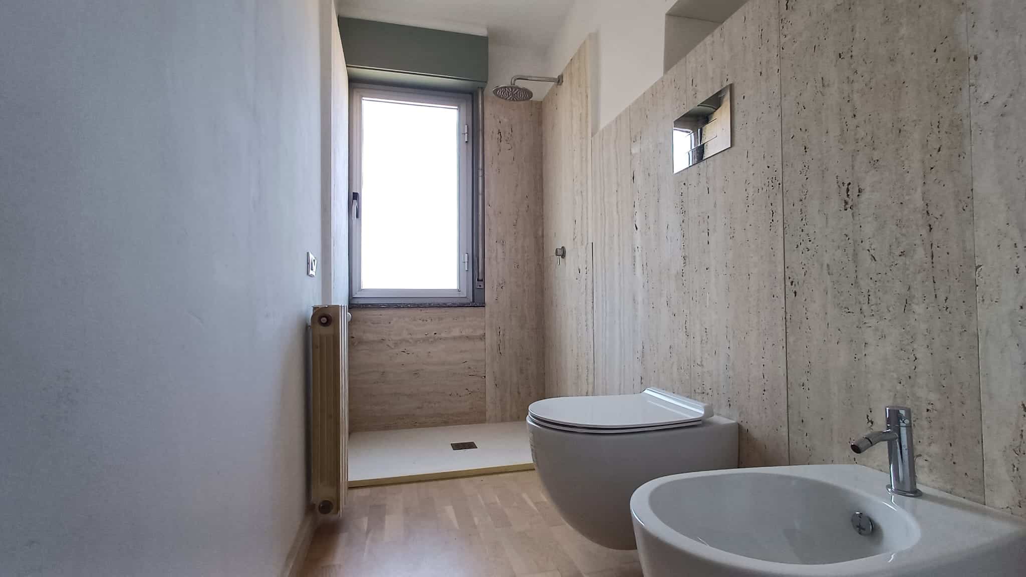 Pannello doccia moderno in bagno con pareti in pietra naturale e finestra luminosa, ideale per ambienti di design e funzionali.