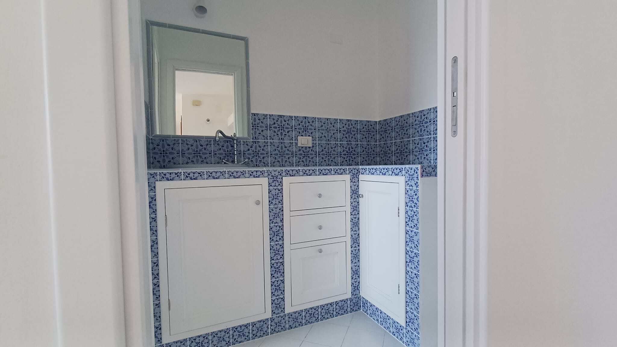 Spazio bagno con mobili bianchi e rivestimento in piastrelle blu, moderno e funzionale, ideale per ambienti di casa eleganti e pratici.